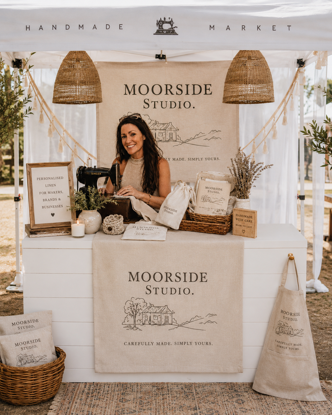 Laura at the Moorside Studio market stall — branded linen runner, banner, apron and cushions under a Handmade Market canopy